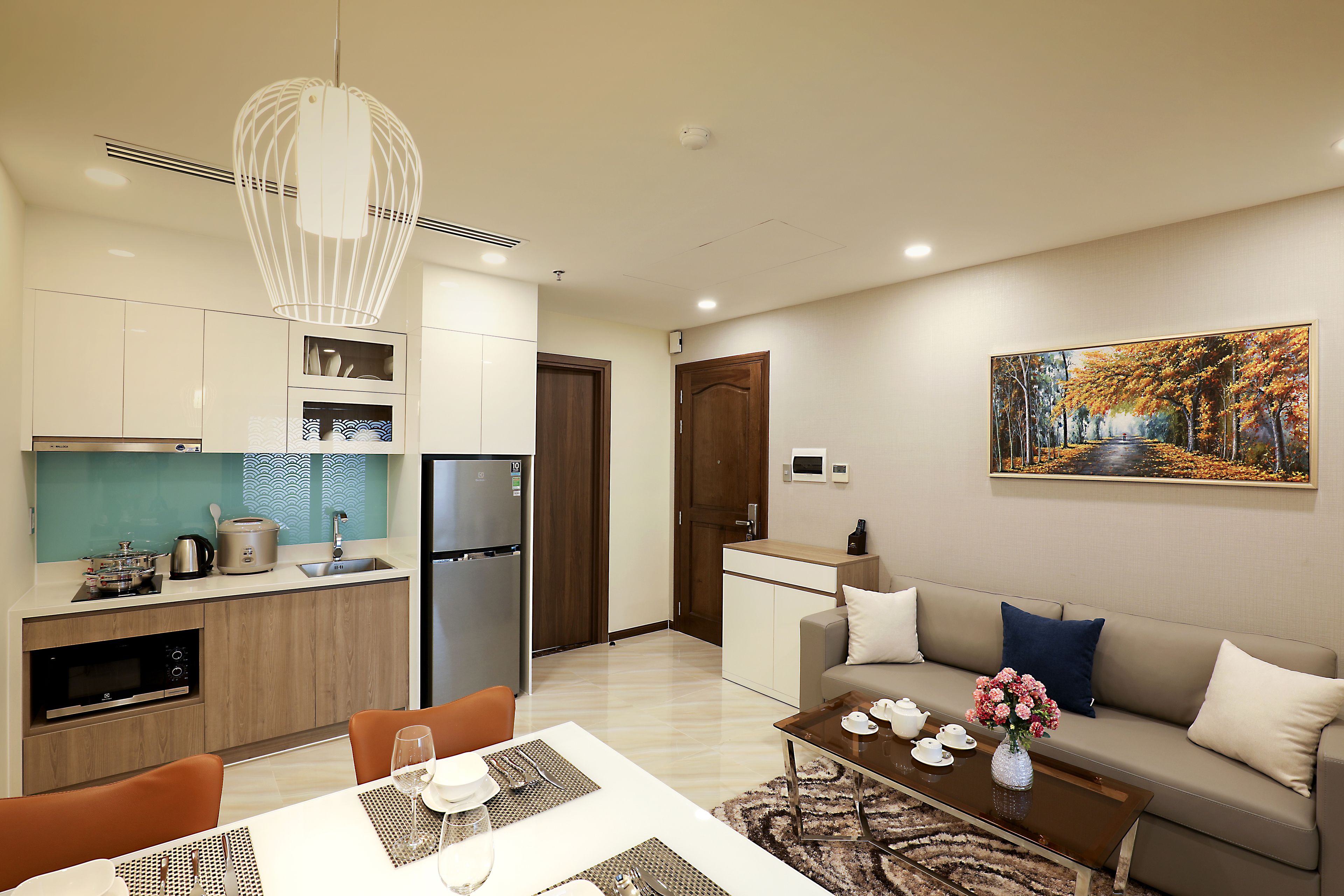 A modern apartment with a kitchen, dining area, and living room. It includes a refrigerator, microwave, and dining table with chairs.