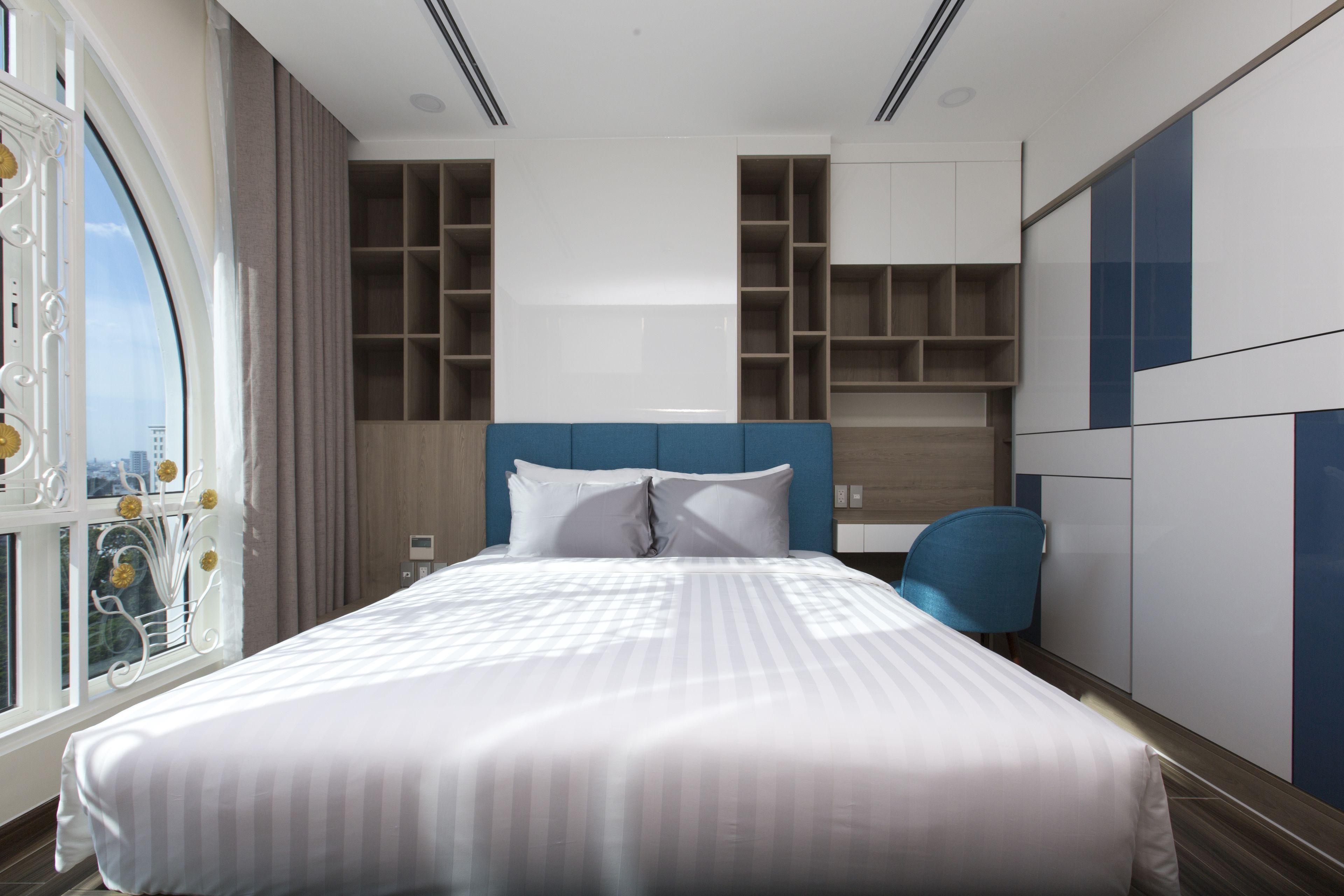 Ein modernes Hotelzimmer mit einem großen Bett, eingebauten Regalen und Blick durch ein Fenster.