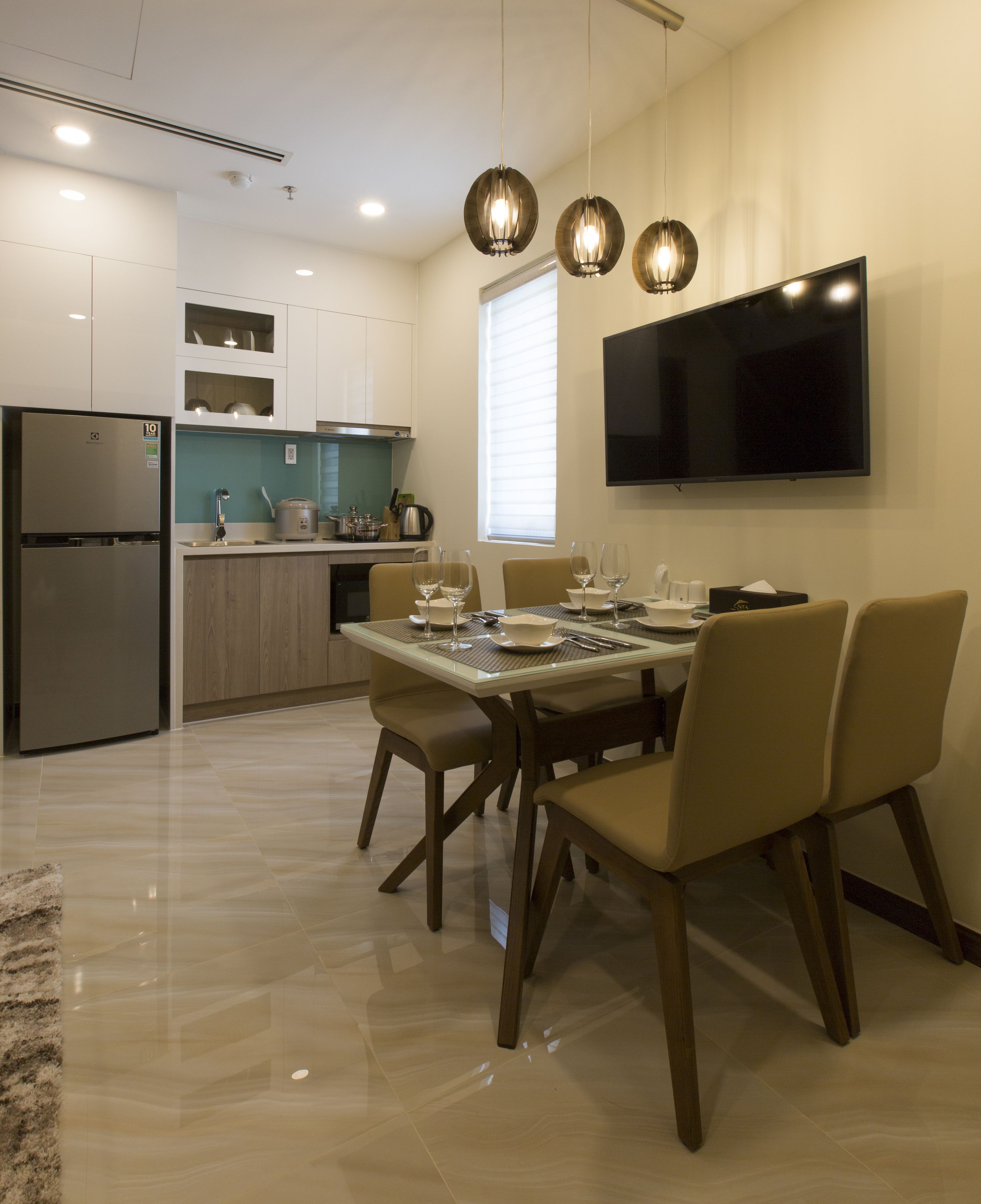 A modern kitchen with a built-in refrigerator, a dining table set for four, and a flat-screen TV mounted on the wall.