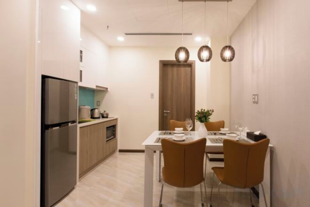 A modern kitchen with a built-in refrigerator, wooden cabinets, and a dining area with a white table and two chairs.
