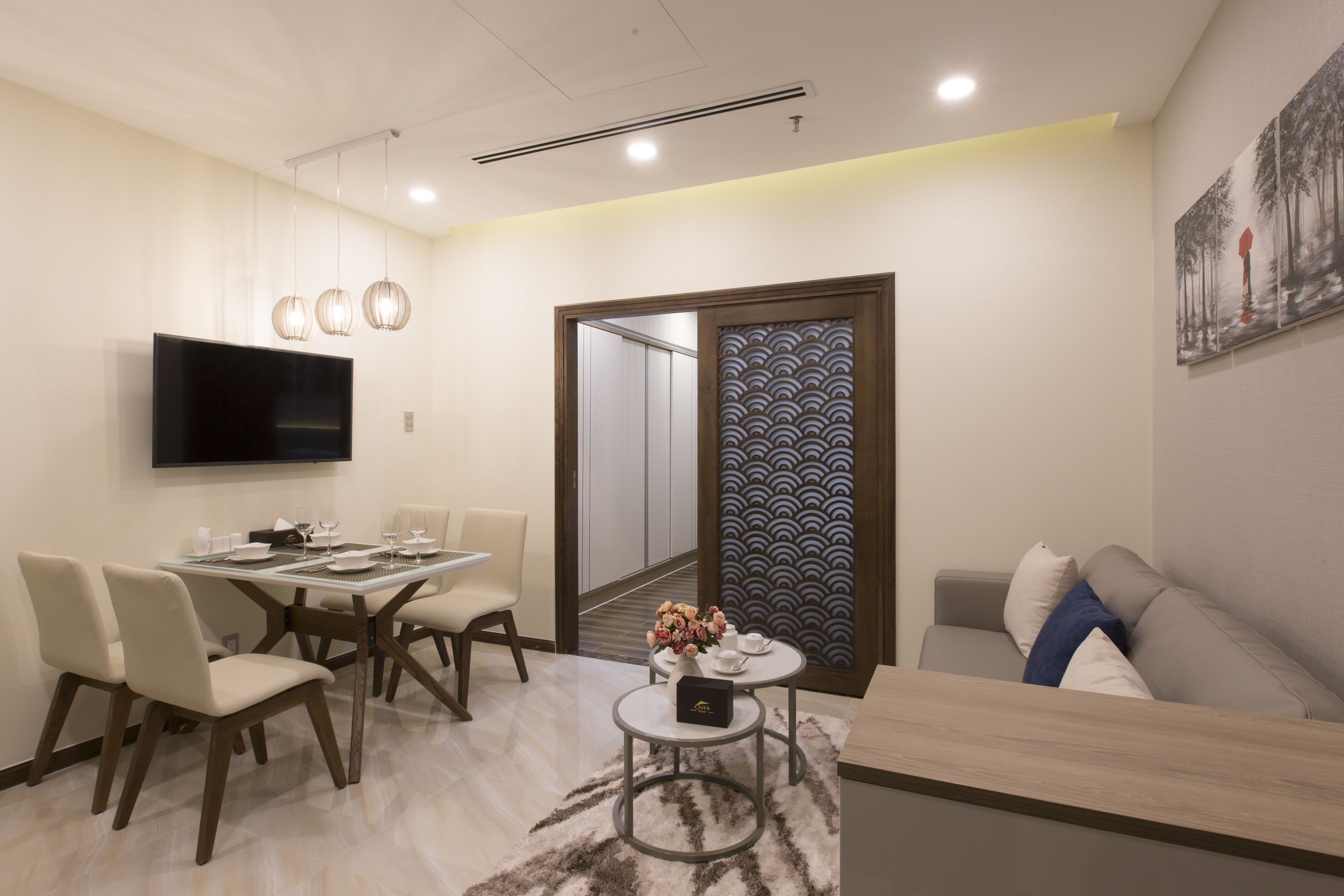 A modern living room with a flat-screen TV, a dining area with a table and chairs, a sofa, and a decorative wall panel.