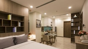 Una habitación de hotel moderna con una cama grande, un escritorio con sillas, una kitchenette y una estantería.