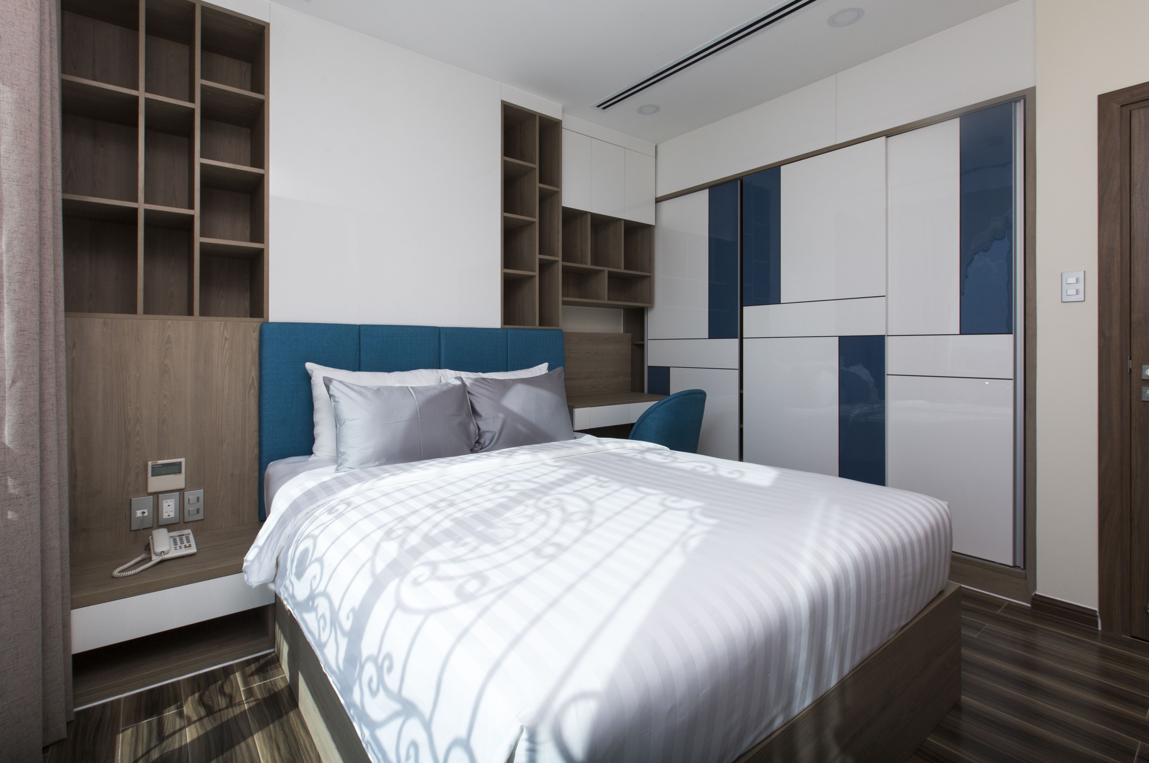Une chambre d’hôtel moderne dotée d’un grand lit, d’étagères intégrées et d’une armoire au design géométrique.