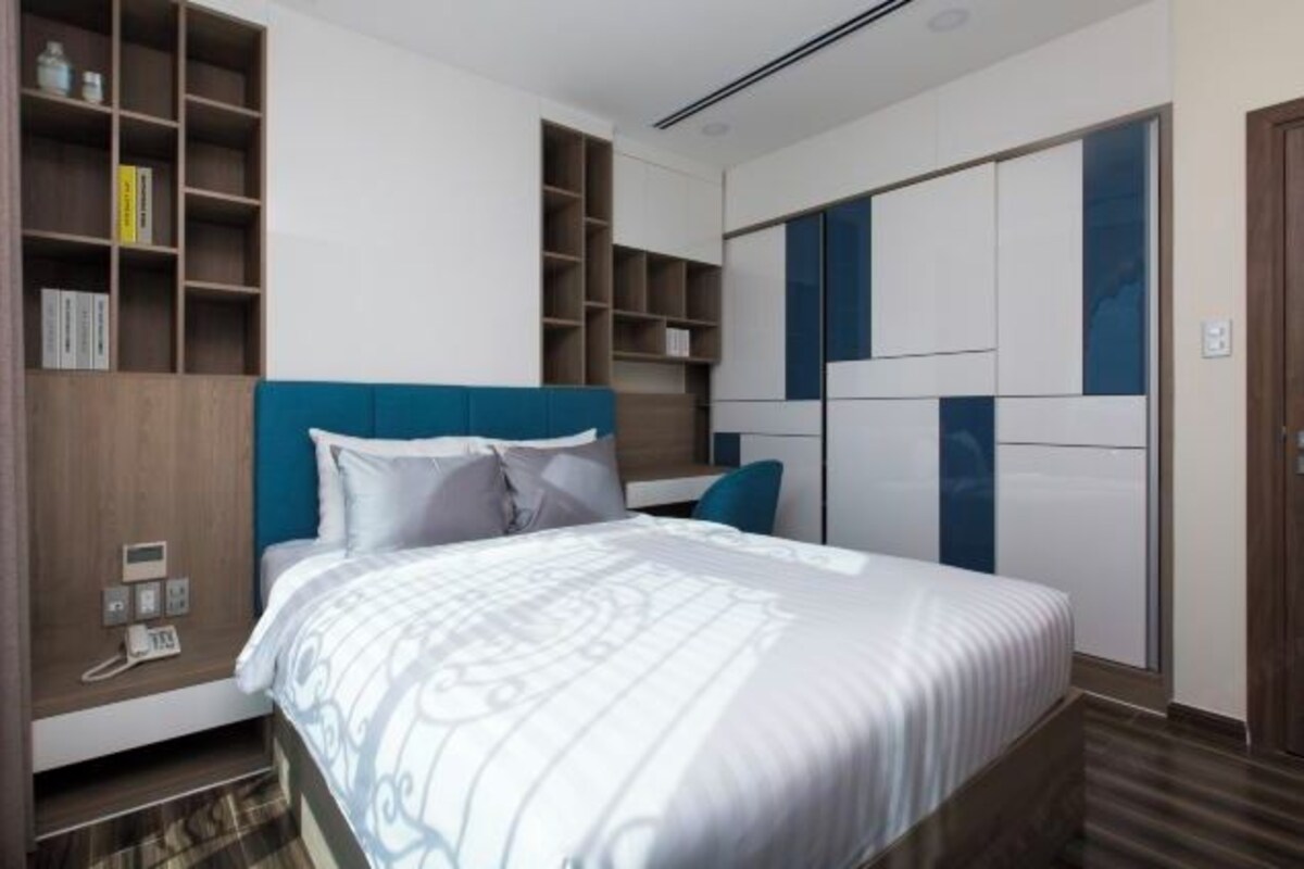 Habitación de hotel moderna con una cama grande, estanterías empotradas y un armario con puertas correderas.