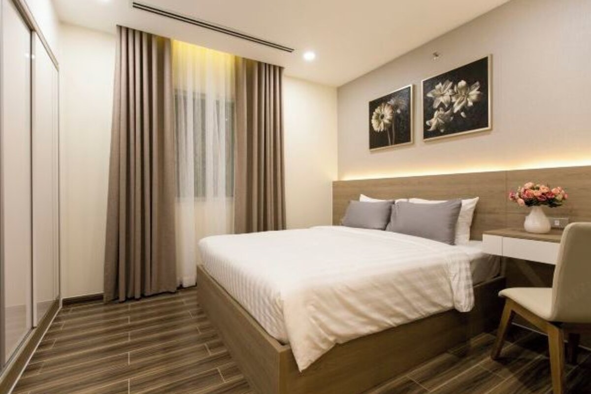 Una habitación de hotel moderna con una cama grande, una mesita de noche con un florero y una silla.