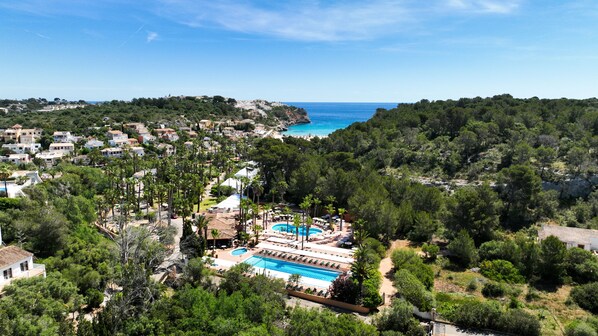 A resort with a large pool, surrounded by lush greenery and a view of the sea. - Flipflop Cala Romántica Hotel (Manacor)