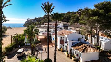 Una propietat costanera amb vistes a la platja, edificis blancs amb teulades vermelles i palmeres.