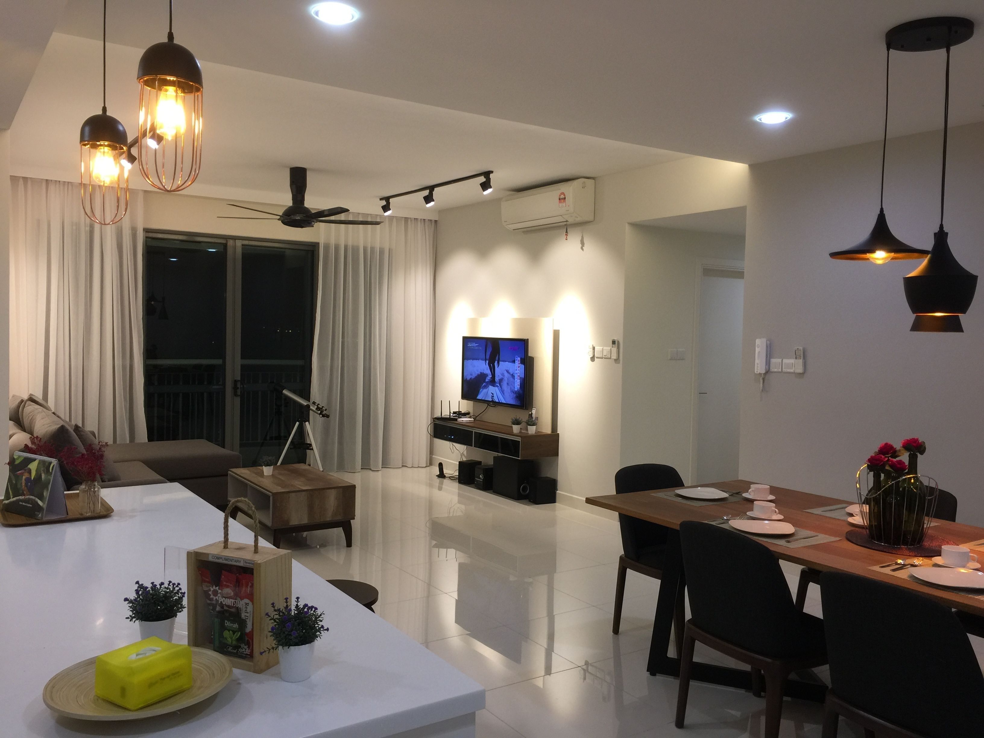 Uma sala de estar moderna com uma TV de tela plana, área de jantar com mesa de madeira e um ventilador de teto.