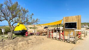 A beachside wooden structure with a yellow canopy, outdoor seating, and a view of the beach. - Cozy Seaside House with Garden, WiFi, 300m to Beach (Bretignolles-sur-Mer)