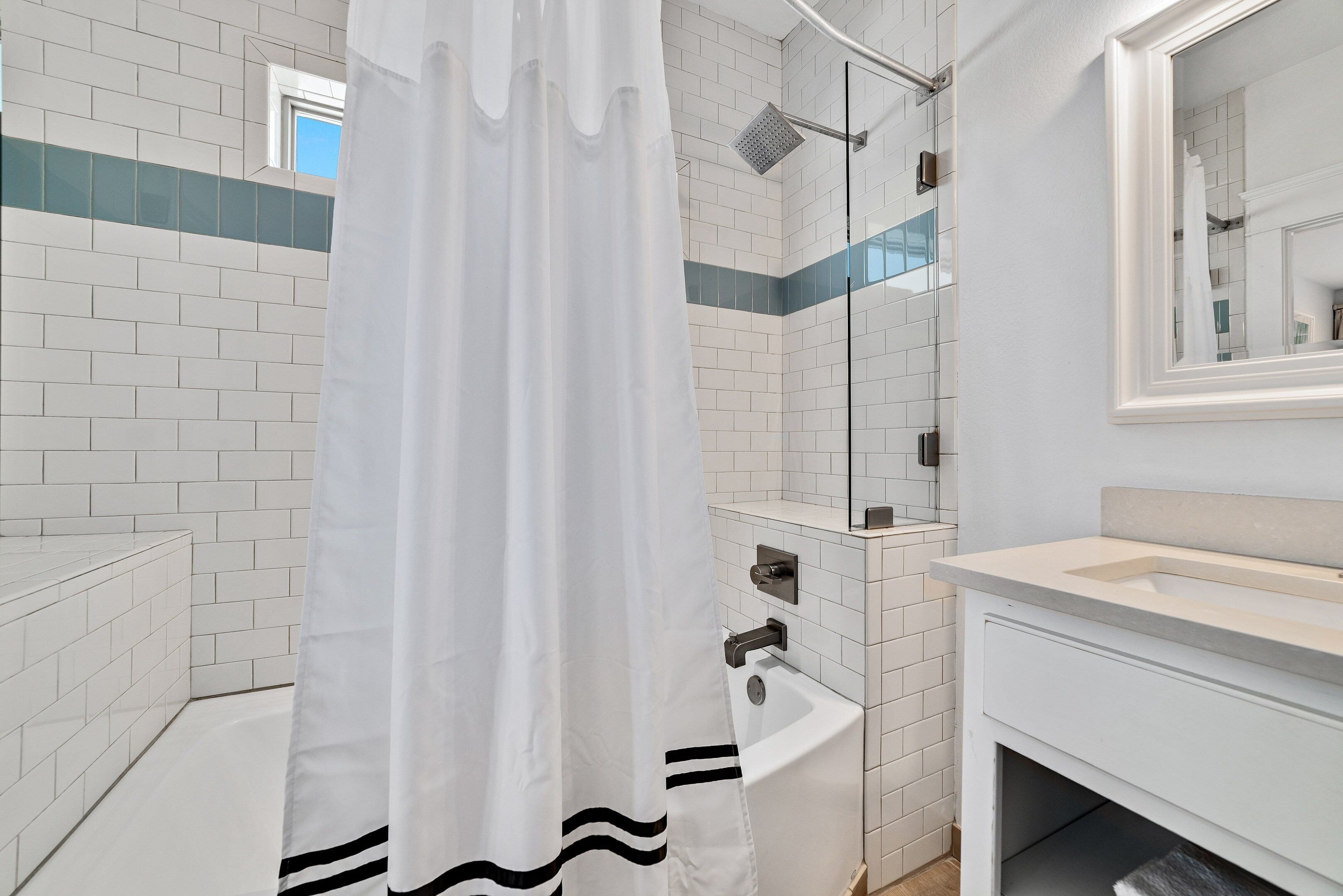 Un baño moderno con paredes de azulejos blancos, una ducha con puerta de cristal y un lavabo con espejo arriba.