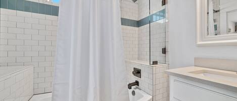 Un baño moderno con paredes de azulejos blancos, una ducha con puerta de cristal y un lavabo con espejo arriba.