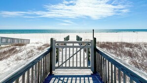 Een houten looppad leidt naar een strand, met een heldere lucht.