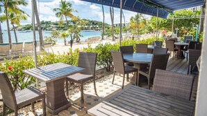 Une terrasse extérieure aménagée avec des meubles en osier, un sol carrelé et une vue sur la plage et l’océan.