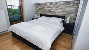 A modern bedroom with a wooden floor, a large bed with white linens, a stone-patterned headboard, and a nightstand with a lamp. - City of the Kings Green Silence Apartment (Kraków)