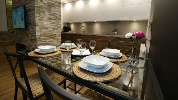 A modern dining area with a glass table set for four, surrounded by wicker chairs. - City of the Kings Green Silence Apartment (Kraków)