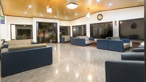 A spacious lobby with modern seating, large windows, and a wooden ceiling. - The Mountain Quail (Dehradun)