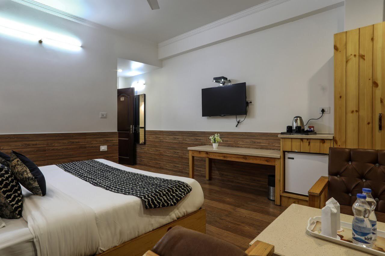 A hotel room with a bed, a television mounted on the wall, a small table, and a cabinet.