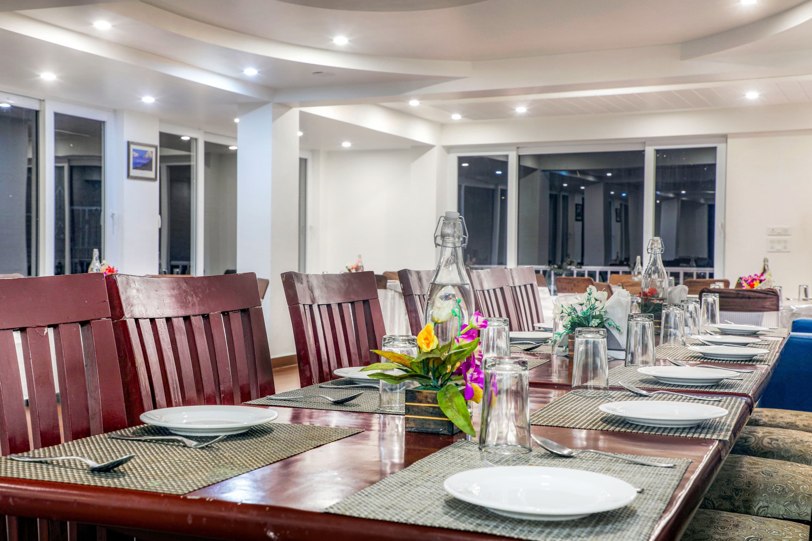 A dining area with a long table set for multiple people, wooden chairs, and a view of the city through large windows.