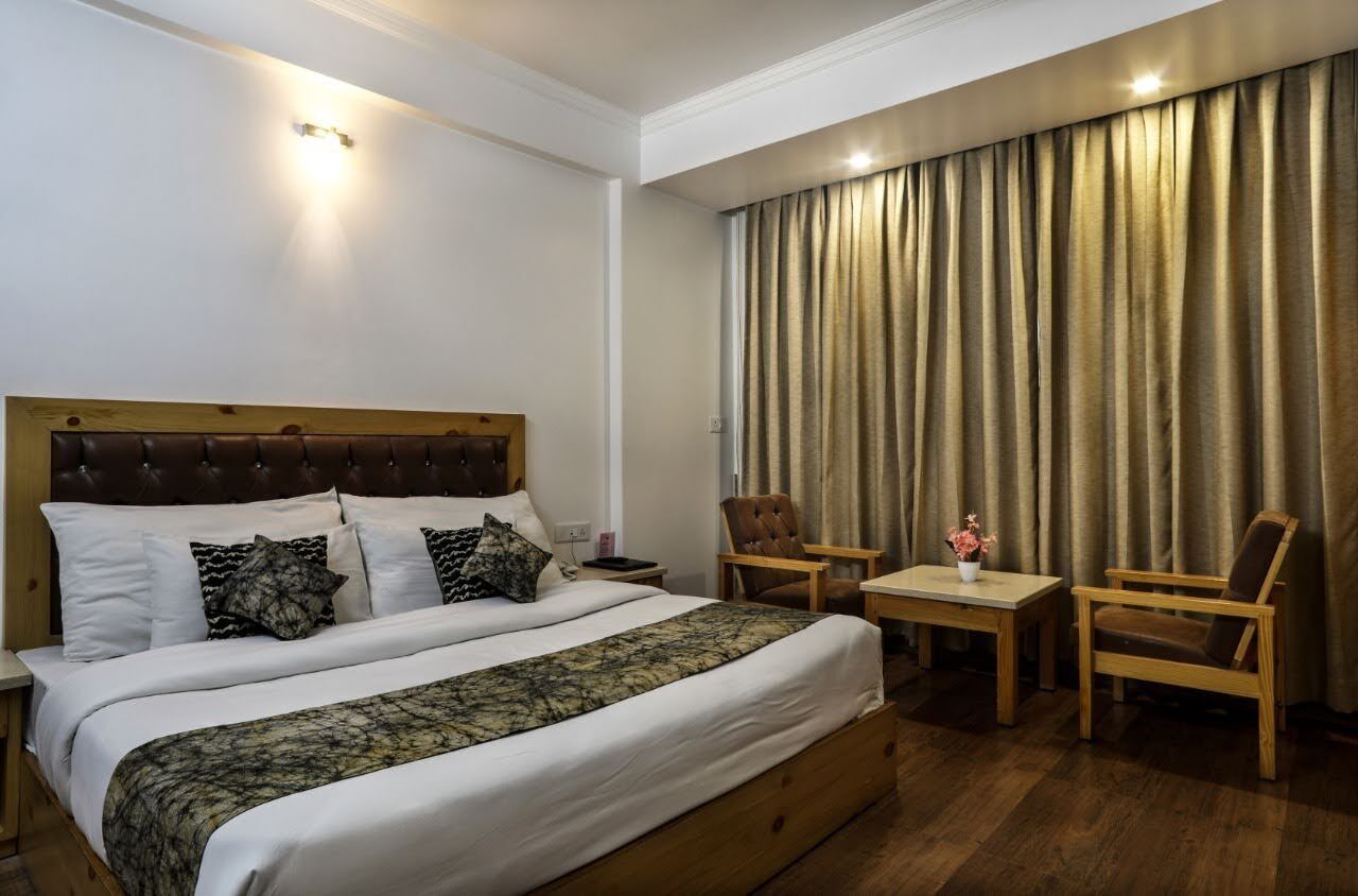 A hotel room with a large bed, two chairs, a small table, and a curtain.