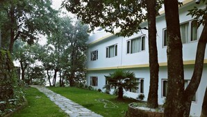 A building with a stone pathway leading to a grassy area, surrounded by trees. - The Mountain Quail (Dehradun)