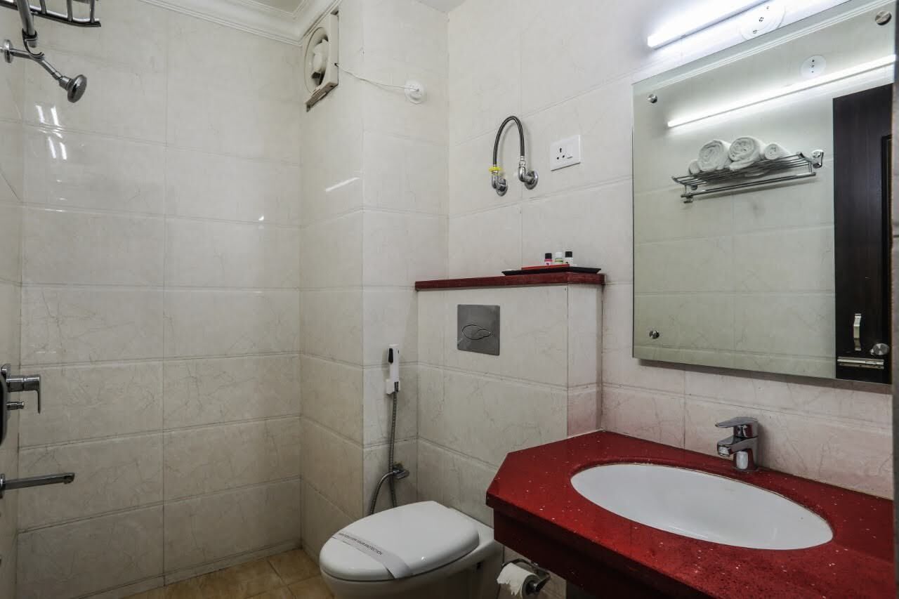 A bathroom with a white toilet, a red sink, a mirror, and a shower area.