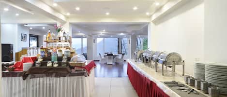 A buffet setup with a variety of food items and beverages, a seating area in the background, and a view of the outdoors.