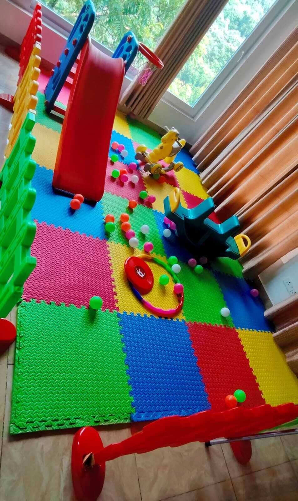 Un área de juegos con piso de espuma entrelazada de colores, un tobogán y diversas estructuras lúdicas.