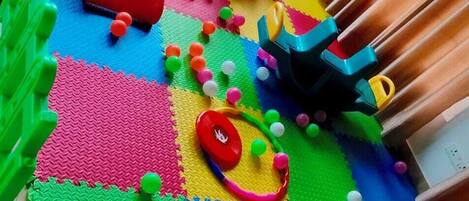 Un área de juegos con piso de espuma entrelazada de colores, un tobogán y diversas estructuras lúdicas.
