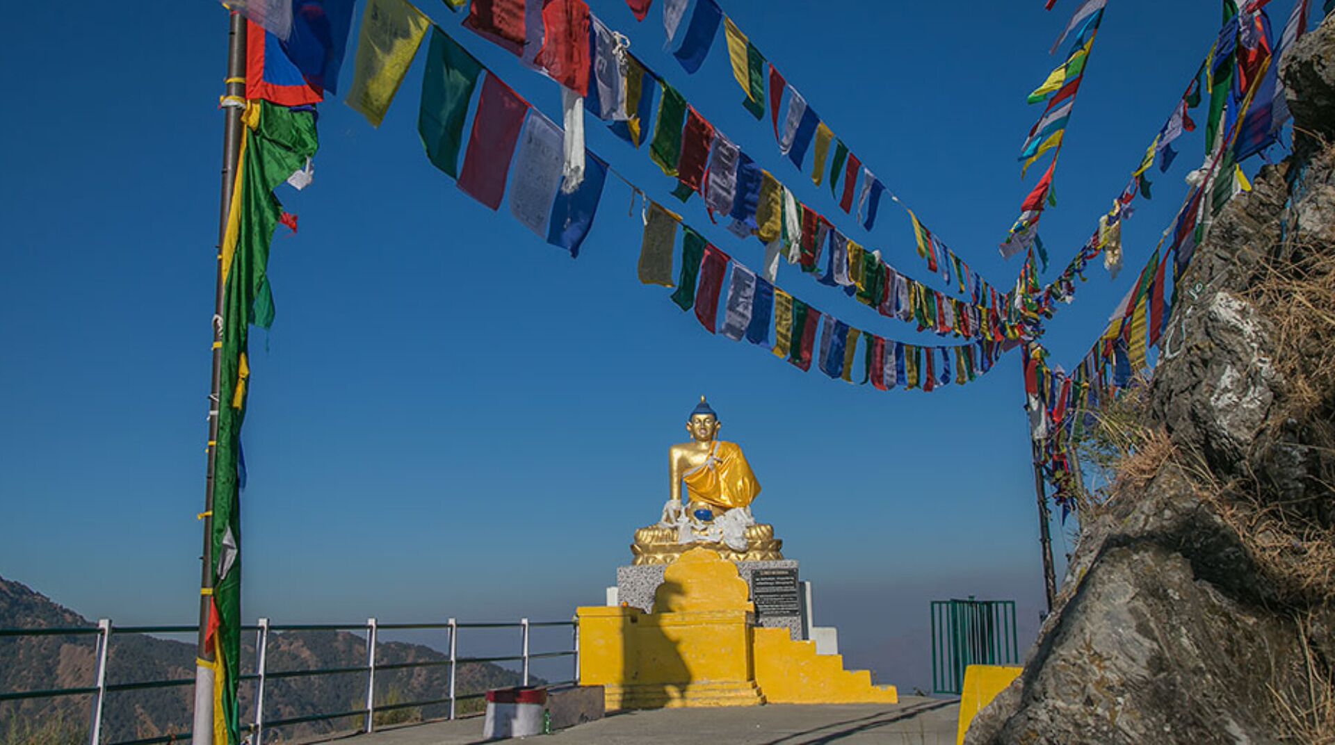 A golden statue of a seated figure on a pedestal, surrounded by colorful prayer flags.