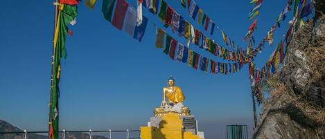 A golden statue of a seated figure on a pedestal, surrounded by colorful prayer flags.