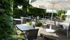 An outdoor seating area with tables and chairs under umbrellas, surrounded by greenery. - Landgasthaus Hotel Eggert (Rheine)