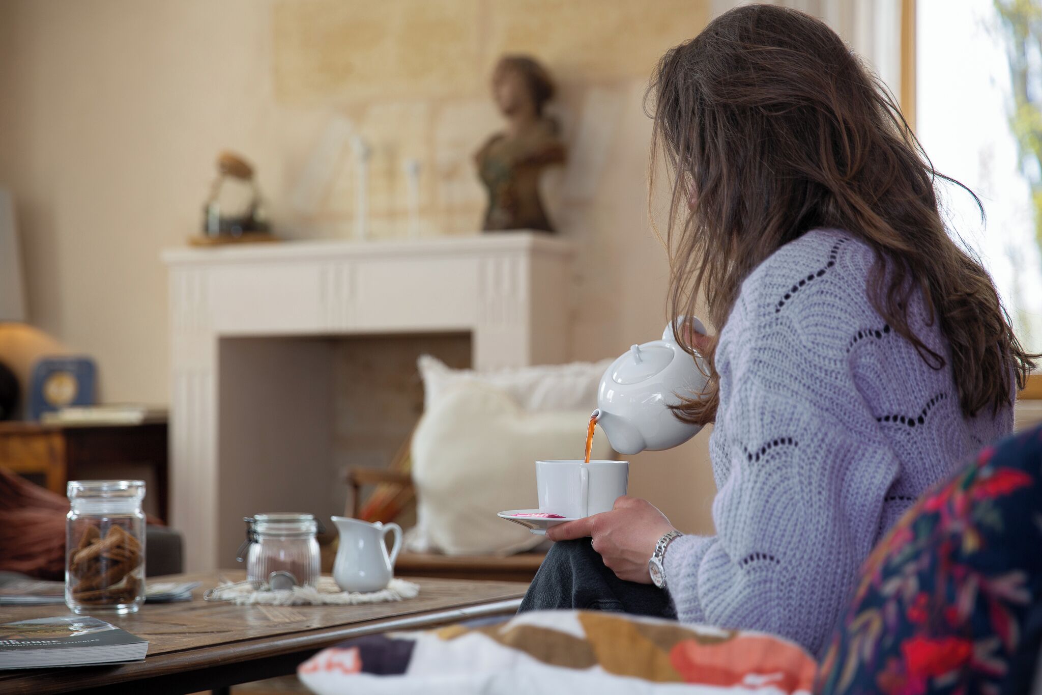 A person holding a cup, seated at a table with a fireplace in the background.