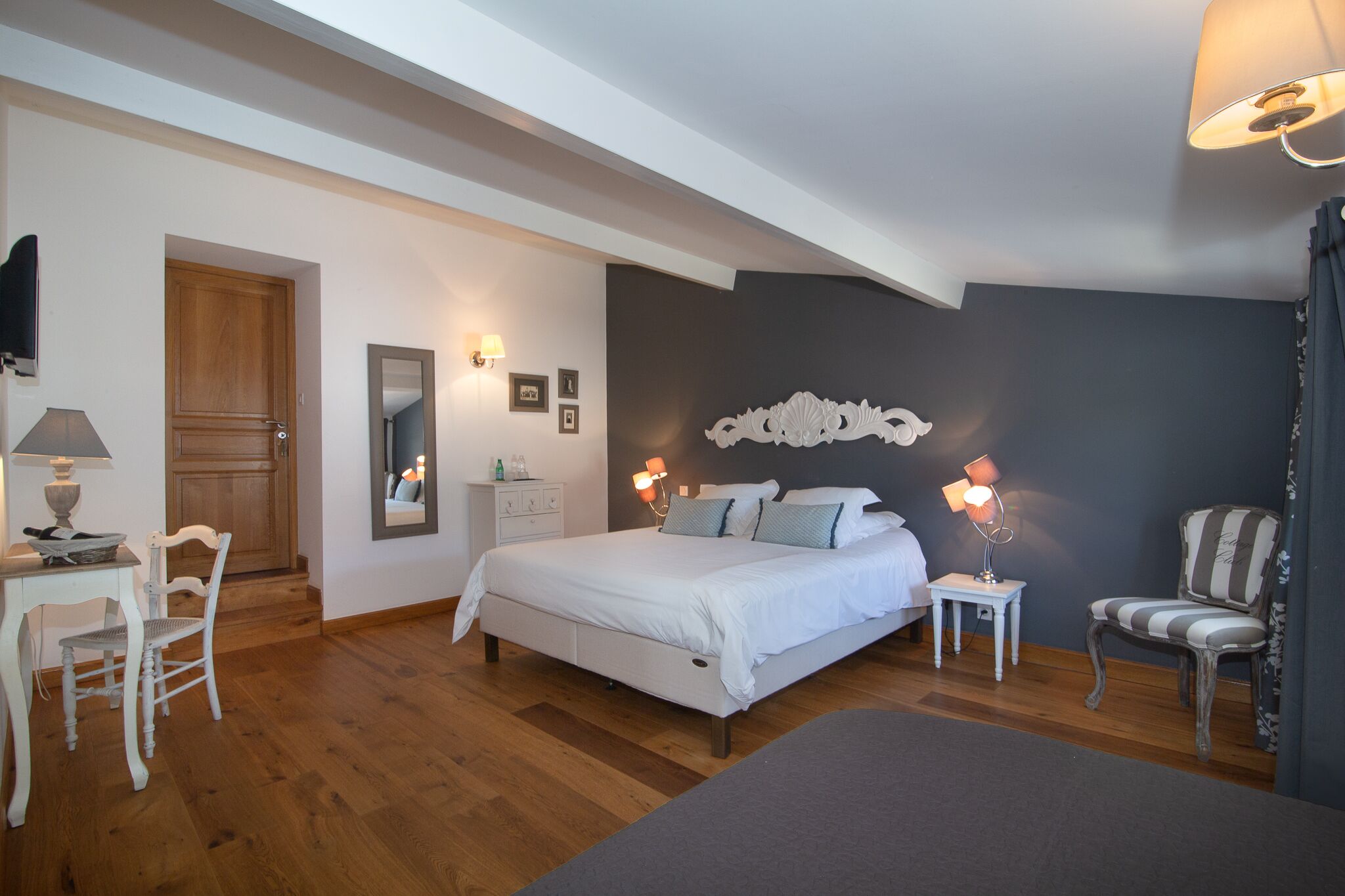 A bedroom with a bed, bedside tables, a chair, a desk, and a mirror.