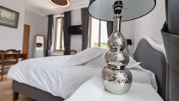 Ein ordentlich bezogenes Bett mit weißen Bettwäsche, eine silberne Vase mit schwarzem Lampenschirm auf einem Nachttisch und ein Holzstuhl im Hintergrund.