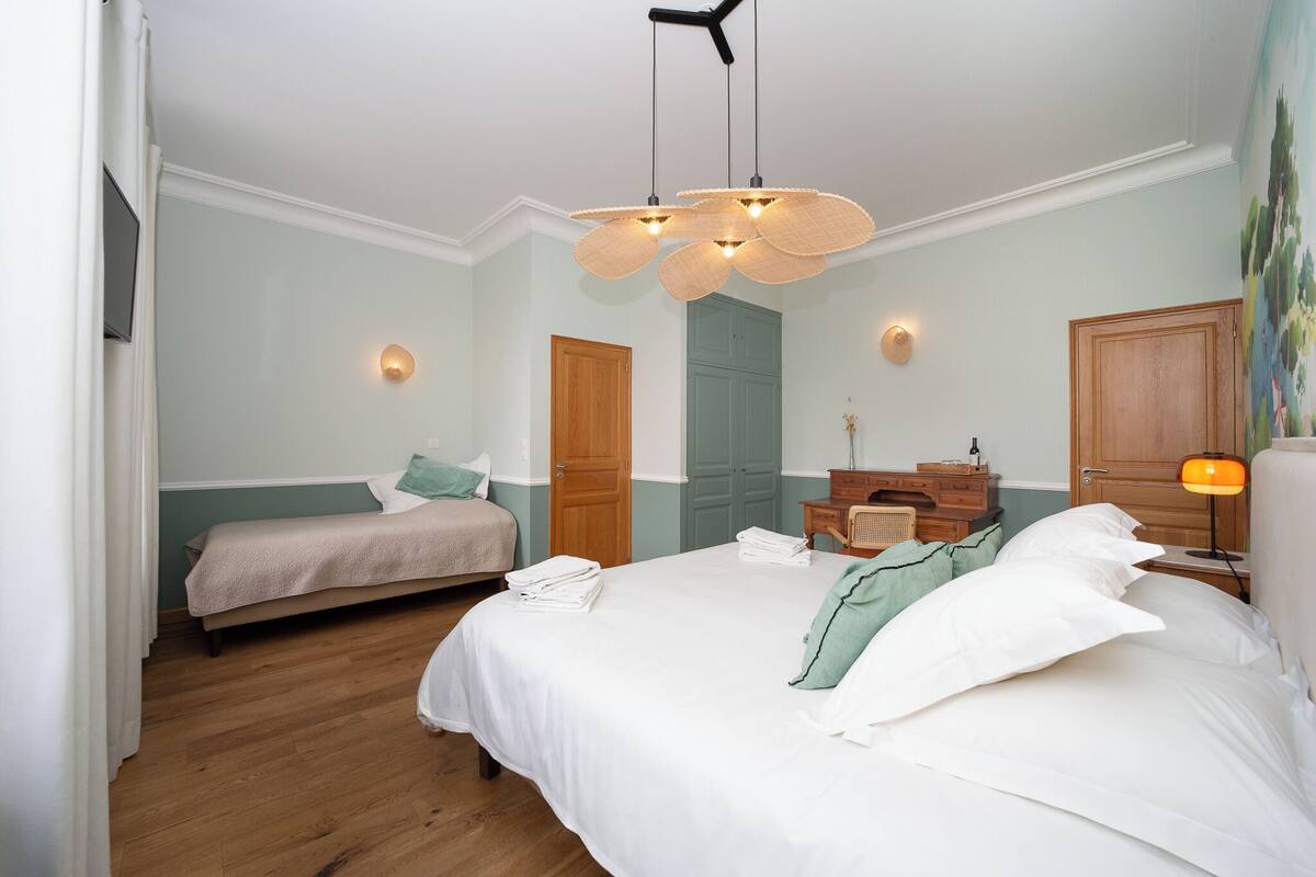 A bedroom with two beds, a wooden dresser, a nightstand, and a ceiling fan.
