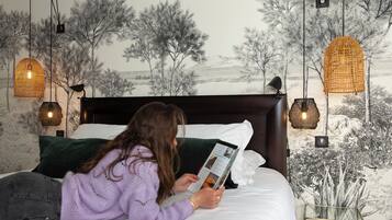 Una persona leyendo un libro en una cama, con un mural de árboles y un paisaje al fondo.