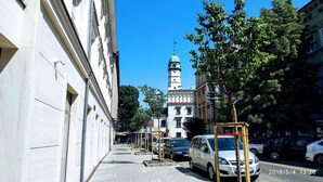 A street with parked cars, a building with a dome and tower, and trees. - City of the Kings City Point Apartments (Kraków)