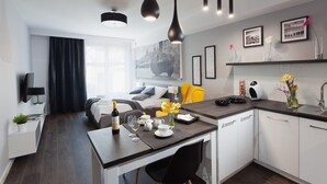 A modern hotel room with a bed, a dining area with a table set for two, a kitchen with a sink and a coffee machine, and a large window with curtains. - City of the Kings City Point Apartments (Kraków)