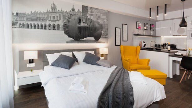 A modern hotel room with a large bed, a bright yellow armchair, a kitchenette, and a wall mural. - City of the Kings City Point Apartments (Kraków)