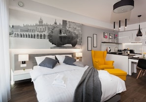 A modern hotel room with a large bed, a bright yellow armchair, a kitchenette, and a wall mural. - City of the Kings City Point Apartments (Kraków)