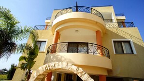 A multi-story building with a curved balcony, a stone archway, and a clear blue sky. - Apartment Emelia (Paphos)