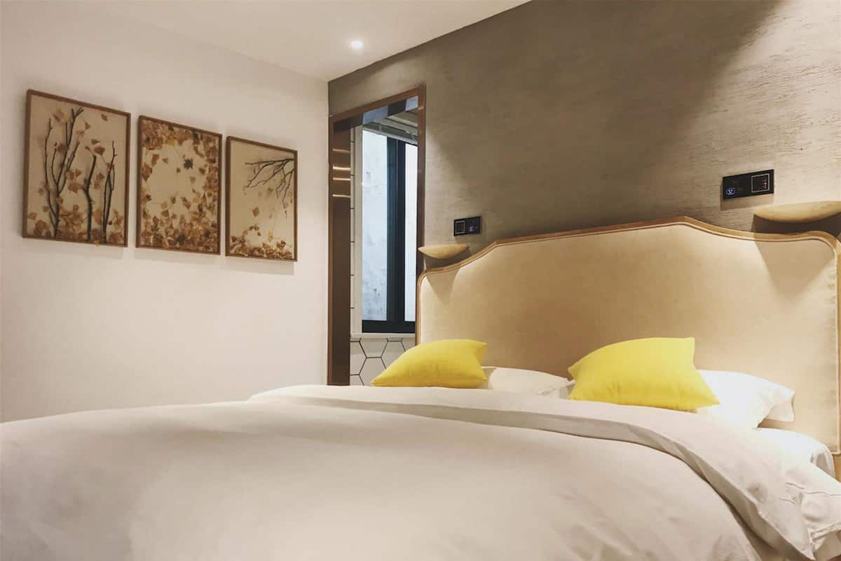 Une chambre à coucher avec un grand lit, deux oreillers jaunes et trois œuvres d’art accrochées au mur, représentant des branches et des feuilles.