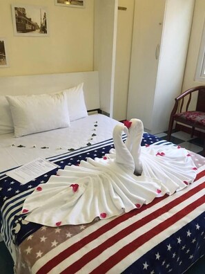 A hotel room with a neatly made bed, a framed picture on the wall, and a wooden chair.