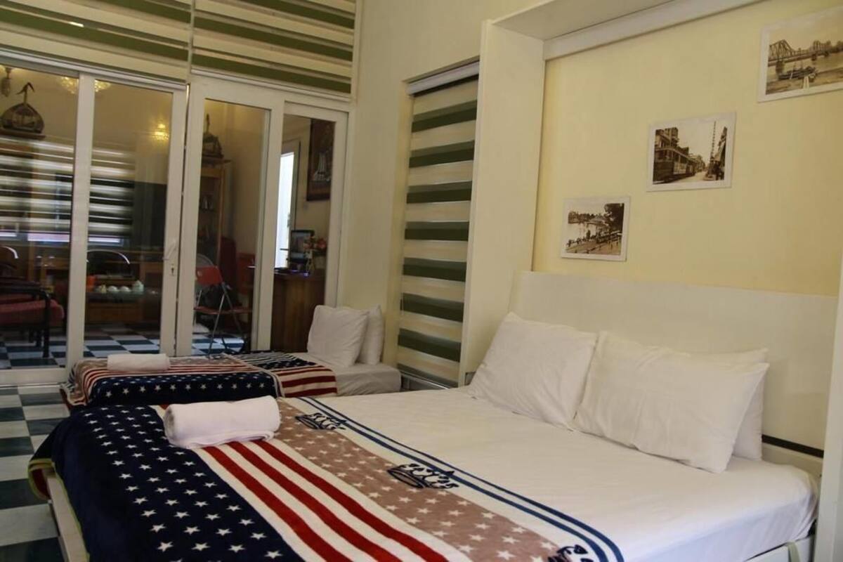 Habitació d'hotel amb dos llits, un amb estovall amb bandera estatunidenca i l'altre amb roba de llit blanca. Hi ha una porta corredissa de vidre que condueix a un balcó amb terra de pissos de graons.