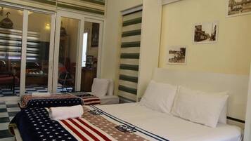 Ein Hotelzimmer mit zwei Betten, eines mit einer Bettdecke mit amerikanischer Flagge und das andere mit weißen Laken. Eine Glastür führt auf einen Balkon mit kariertem Boden.