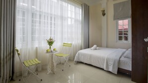 A neatly arranged bedroom with a bed, a chair, a small table with a plant, and a window with curtains. - An Family Homestay (Hanoi)