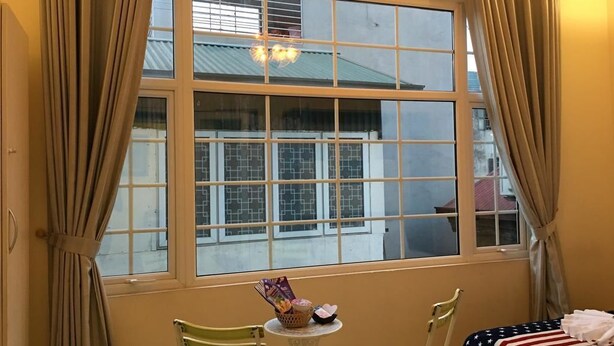 A room with a large window, two chairs, a small table, and a bed with an American flag bedspread. - An Family Homestay (Hanoi)