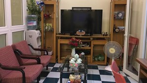 A living room with a TV, two red chairs, a glass coffee table with decorative items, a fan, and a water dispenser. - An Family Homestay (Hanoi)