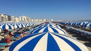 A beach with rows of blue and white striped umbrellas and lounge chairs. - Hotel Avila In (Rimini)