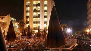 A hotel with multiple floors, outdoor seating with umbrellas, and a well-lit facade. - Hotel Avila In (Rimini)